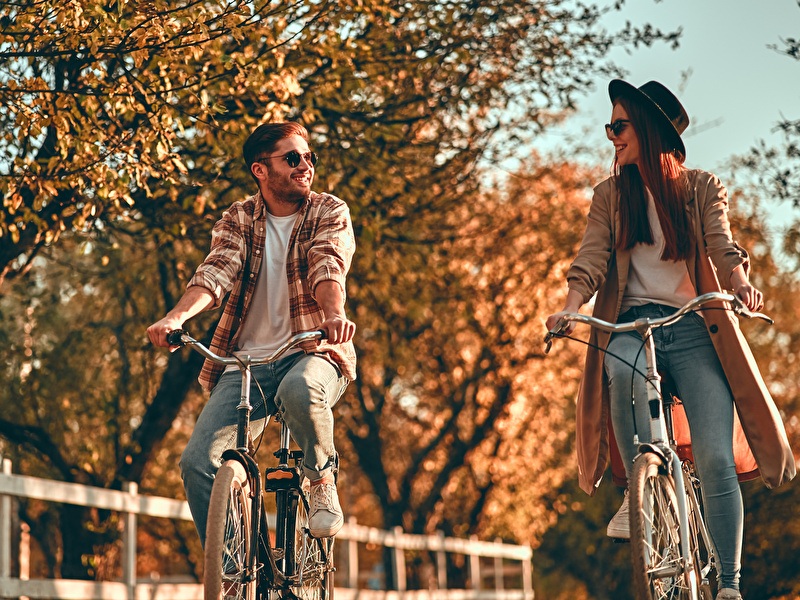 Man en vrouw fietsen lachend naast elkaar op een zonnige herfstdag.