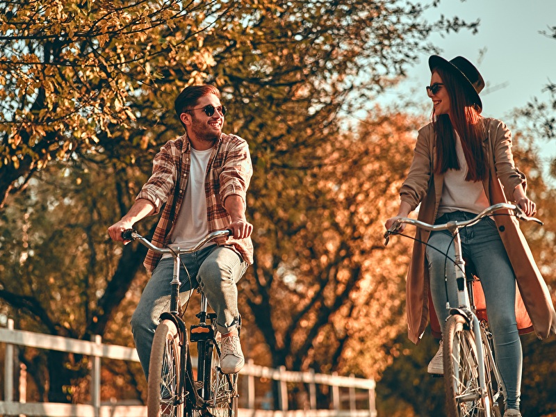 Man and woman cycling laughing side by side on a sunny autumn day.