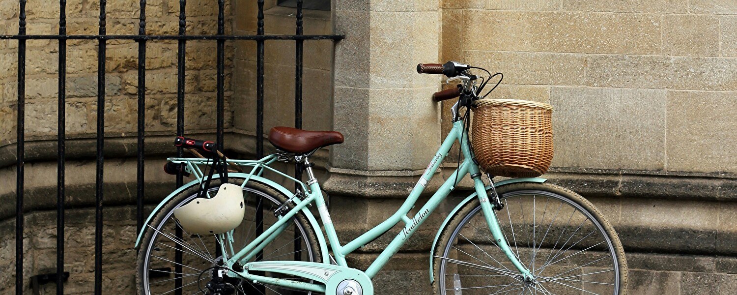 A light green bike parked on the sidewalk leaning against a stone wall.