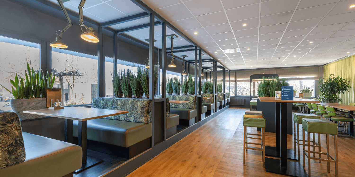 Restaurant in Amrâth Airport Hotel Rotterdam met verschillende zitjes om te werken houten tafels en groene bankjes. Met in het midden van de ruimte nog houten hoge tafels met groene barkrukken