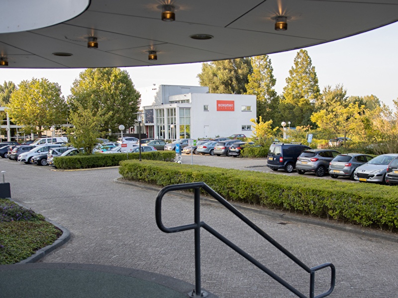 Parkplatz des Amrâth Rotterdam Airport Hotels mit geparkten Autos und umliegendem Grün.