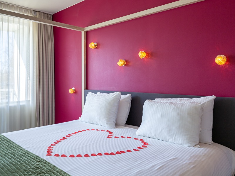 Romantisch dekoriertes Bett mit Rosenblättern in Herzform in einem Hotelzimmer des Amrâth Airport Hotel Rotterdam, mit Blick auf das Wasser.