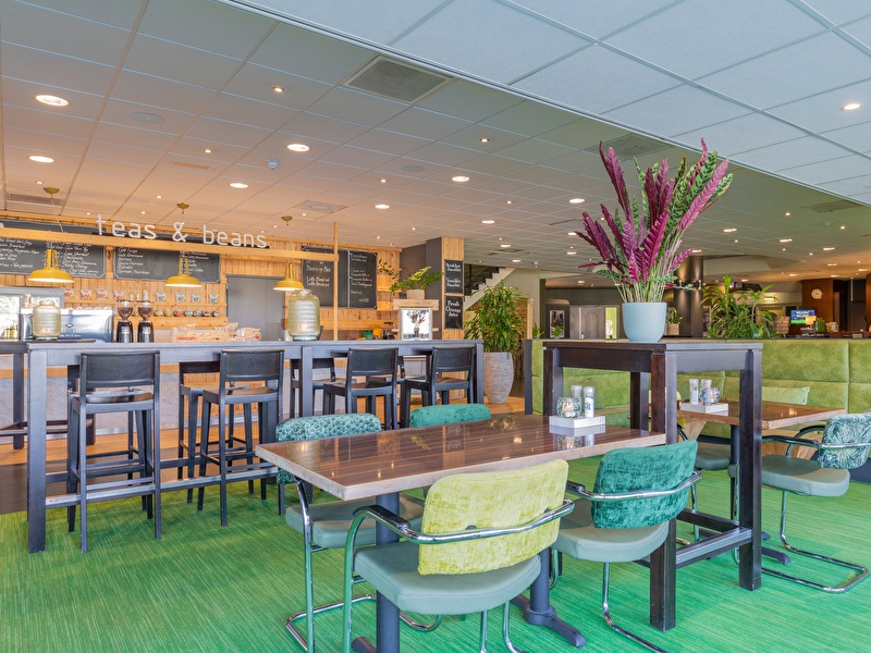 Coffee bar with green carpet and high stools in Amrâth Hotel Rotterdam