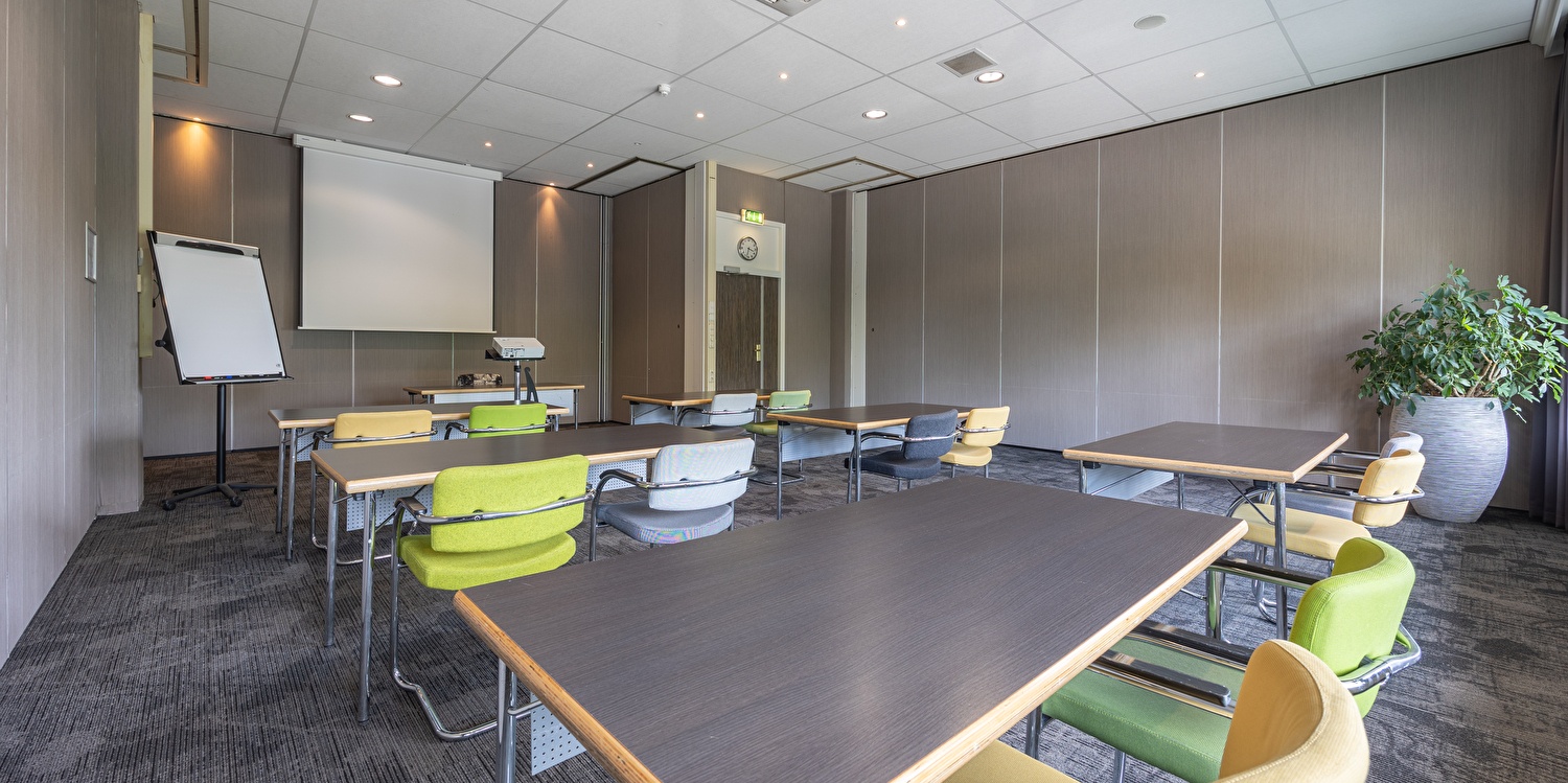Tagungsraum im Amrâth Airport Hotel Rotterdam mit moderner Einrichtung, Beamer, Flipchart und komfortablen Stühlen in einem hellen, professionellen Umfeld.