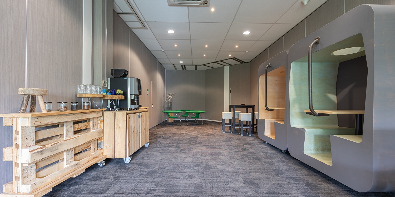 Raum im Amrâth Airport Hotel Rotterdam mit Kaffeebar, Sitzgelegenheiten und modernen Arbeitspods für informelle Besprechungen oder Entspannung zwischen Meetings.