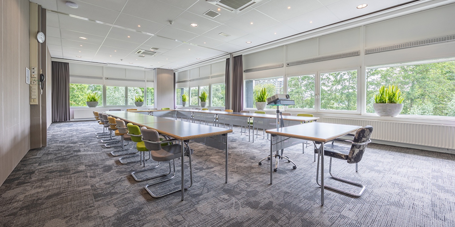 Light and spacious meeting room in Amrâth Airport Hotel Rotterdam with large windows, views of greenery, modern tables and chairs, and a projector for presentations.