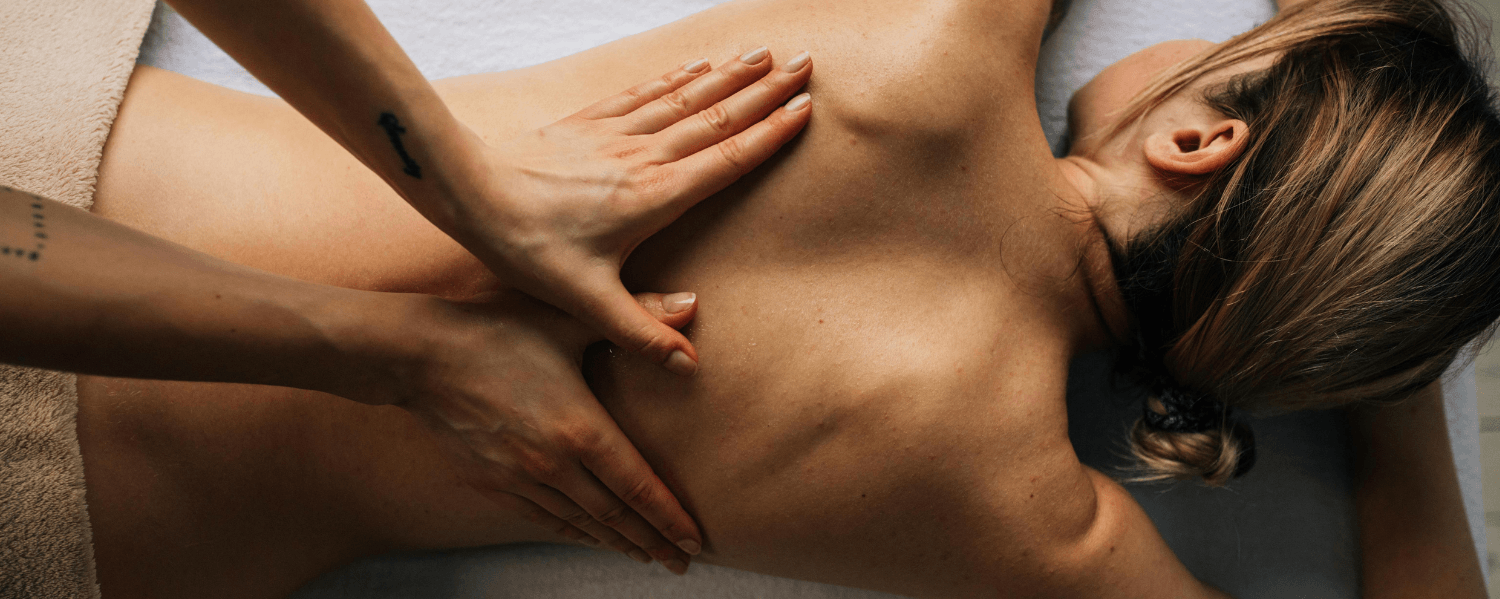 A woman is receiving a back massage, with the masseur focusing on her shoulders and back.